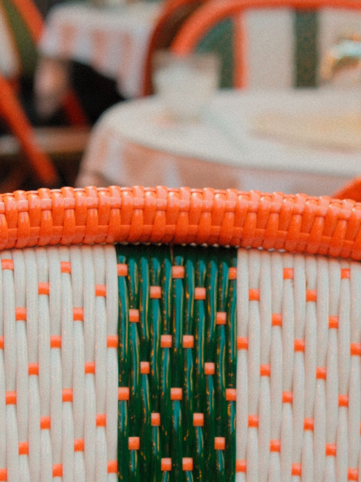 Détail d'une chaise de bistrot tressée orange, blanc et vert