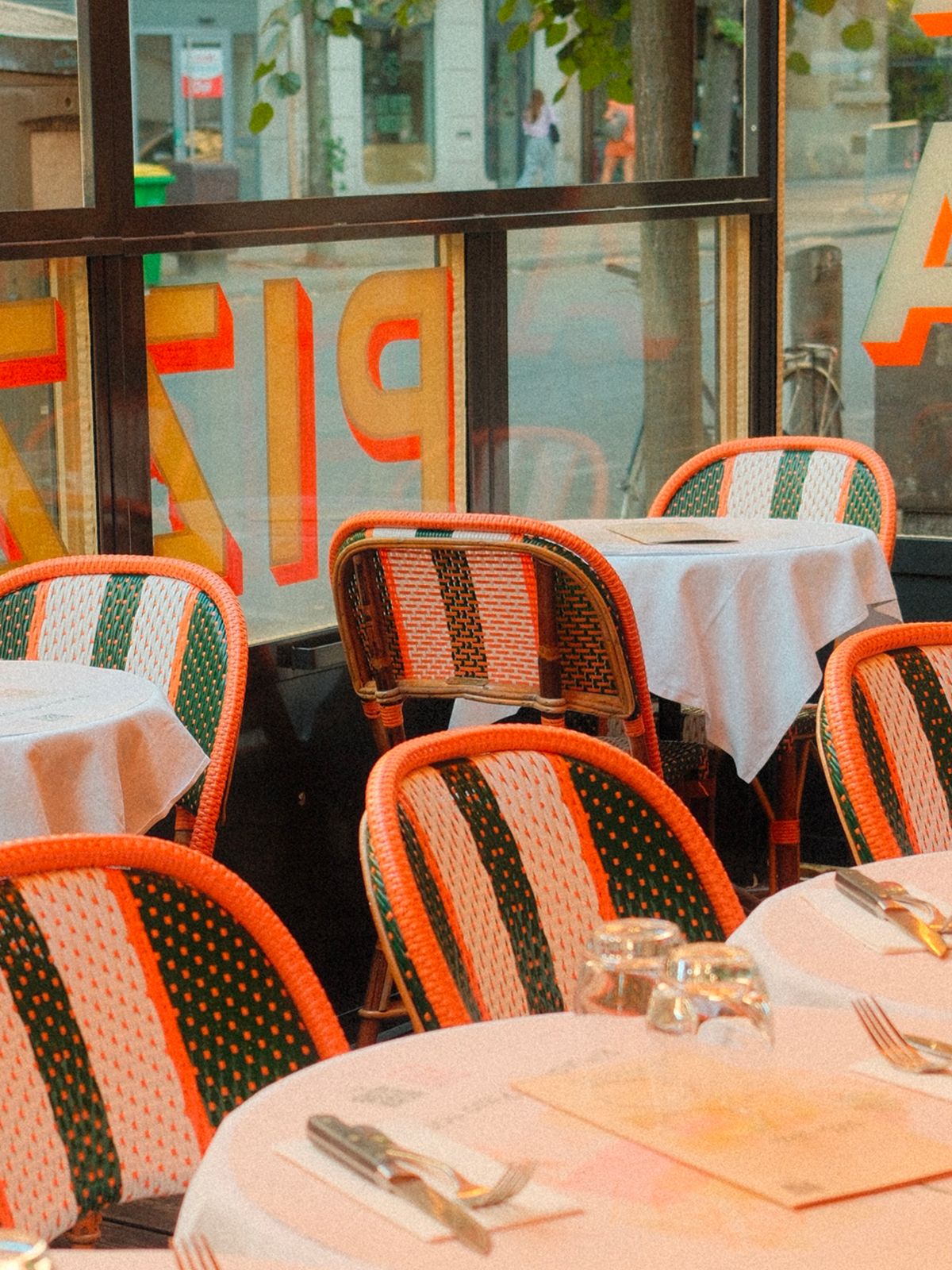 Tables dressées et chaises tressées vert et orange sur la terrasse